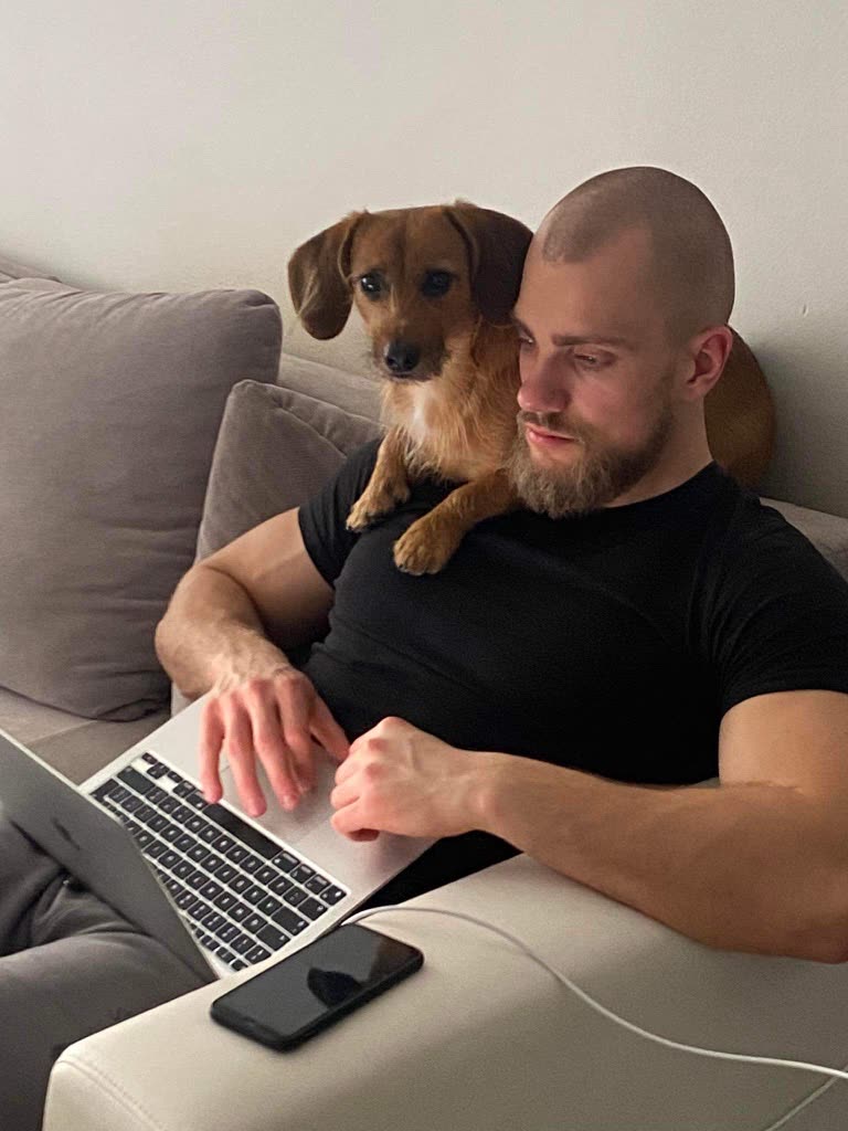 Bartosz Wojciechowski pracuje na laptopie na kanapie, a na jego ramieniu siedzi pies